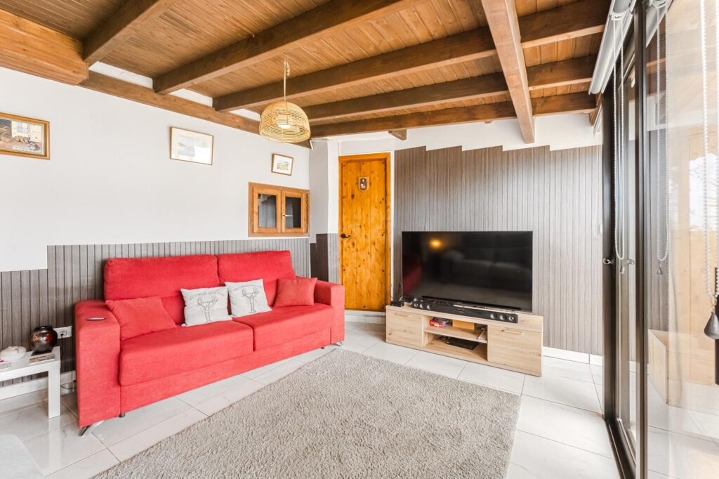 Salón con techos de madera, sofá rojo y mueble de televisor