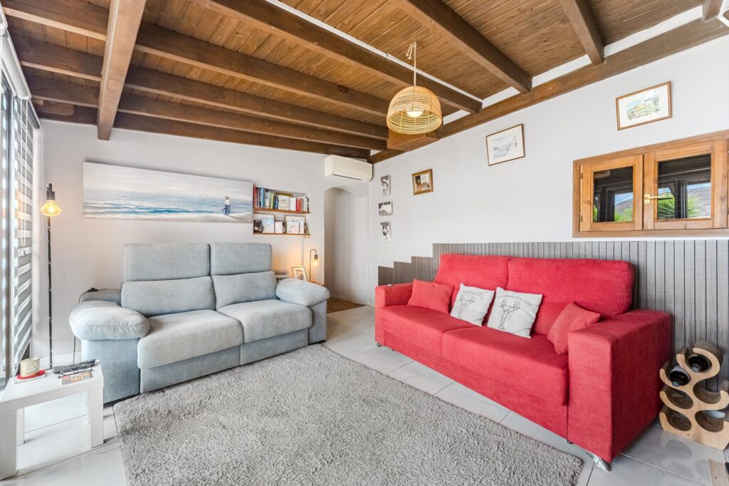 Salón con techos de madera, sofá rojo y otro gris