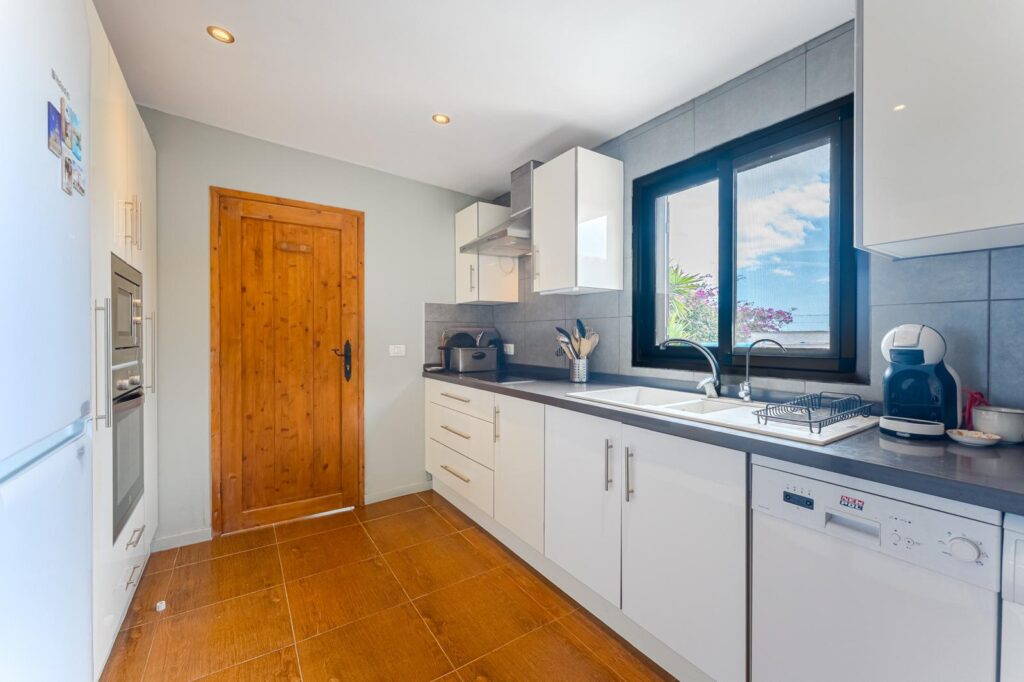 Cocina, puerta de madera natural, muebles claros y ventanas al exterior